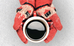 Unes mans amb guants agafant una tassa de café en la neu